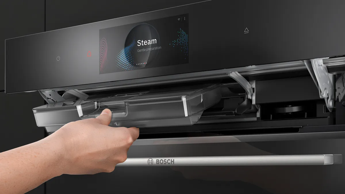 A hand placing the water tank into the steam oven.