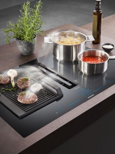 Cocinar electrodomésticos, ollas, hierbas y carne asada en una moderna encimera de cocina.