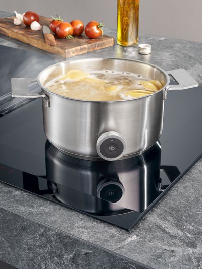 Bote de acero inoxidable en estufa eléctrica con tomates, aceite y otros ingredientes de cocina.