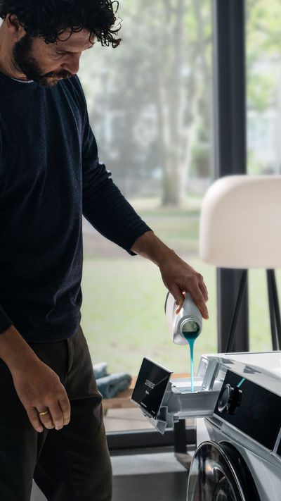 Homem em camisa preta usando máquina de lavar em casa. 