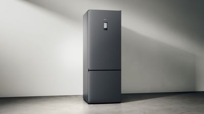 Et elegant, moderne mørkt køleskab med fryser i bunden på en minimalistisk baggrund med blød belysning. 