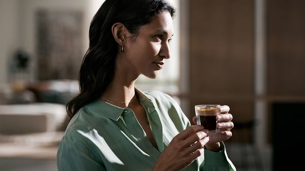En person nyder en espresso, iført en blød skjorte, i et stilrent indendørsmiljø. 