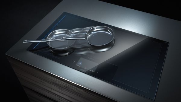 Encimera de inducción elegante y moderna con superficie de vidrio reflectante y utensilios de cocina de metal.